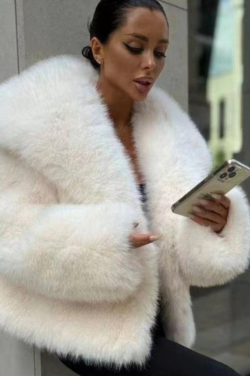 Woman wearing a white fluffy coat holding a phone.