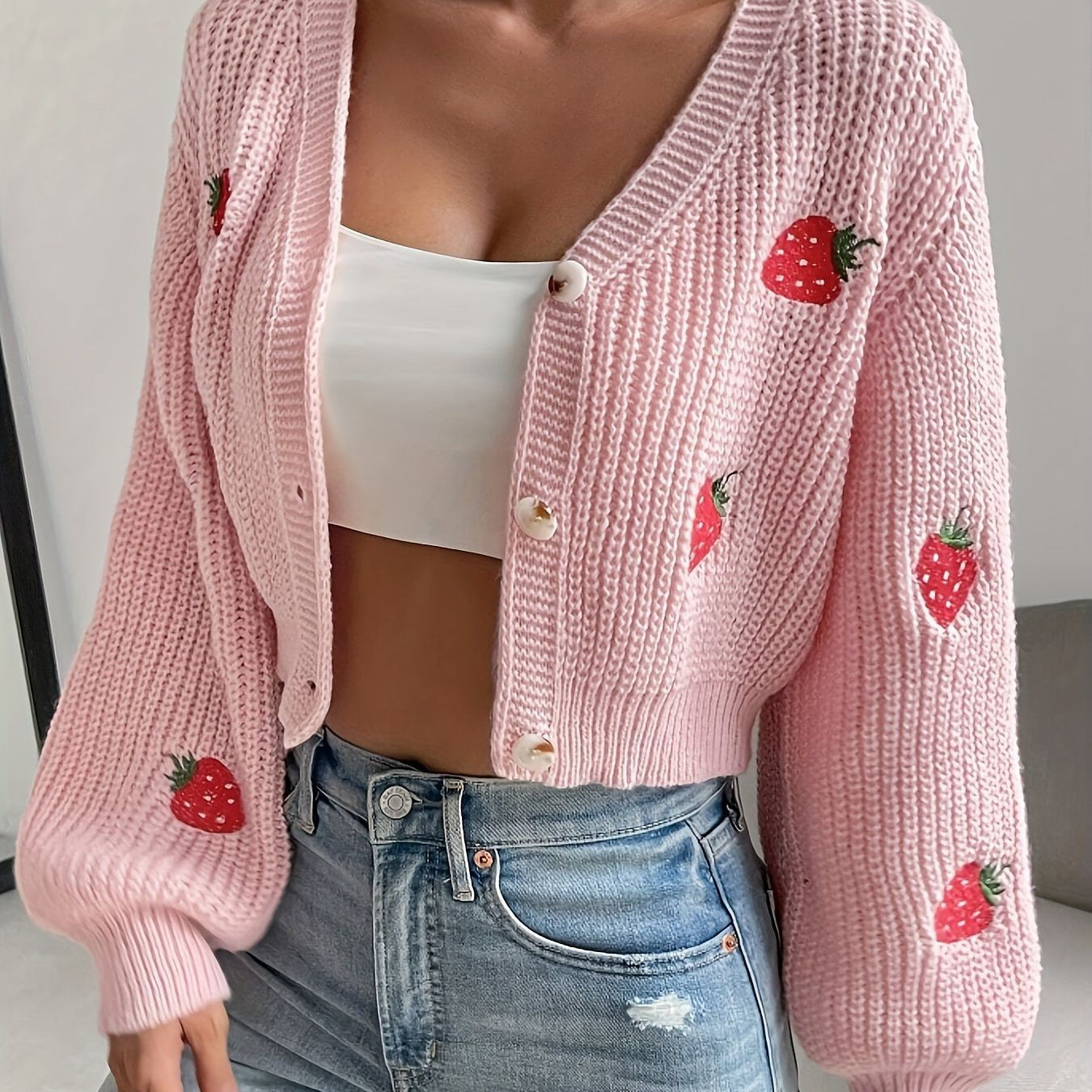 Pink knitted cardigan with strawberry patterns worn by a person, with a white top and blue jeans.