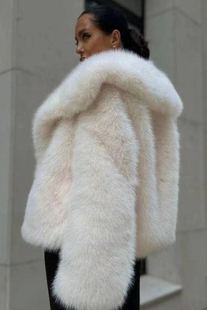 Person wearing a white fur coat standing against a neutral wall.