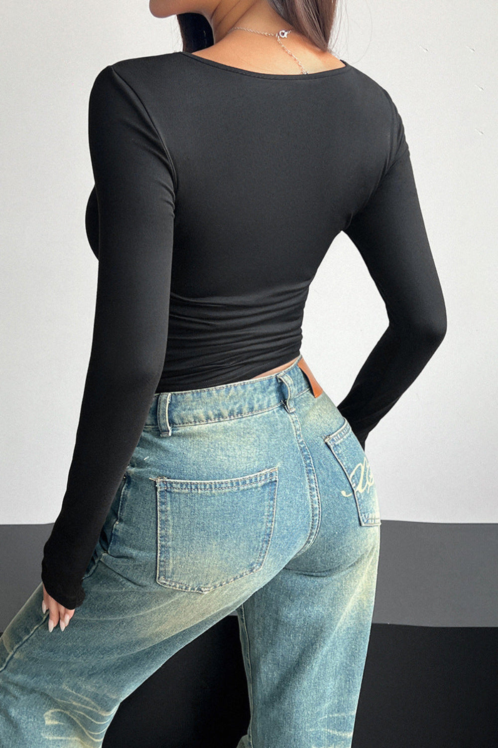 Person wearing a black long-sleeve top and blue jeans against a plain background