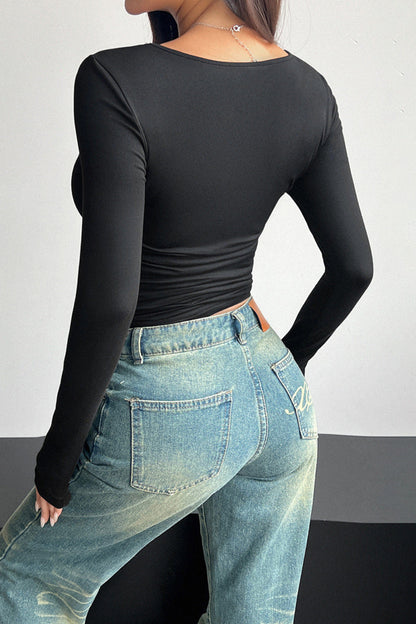 Person wearing a black long-sleeve top and blue jeans against a plain background