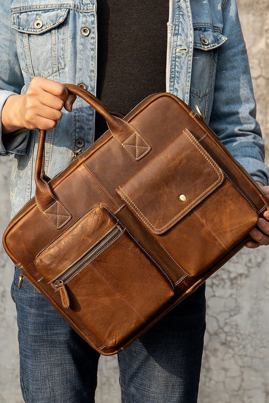 Person holding a brown leather briefcase against a textured wall.
