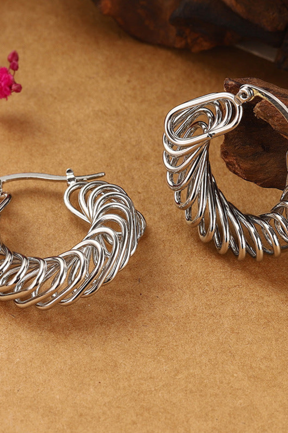 Silver hoop earrings on a brown surface with dried flowers and wood.