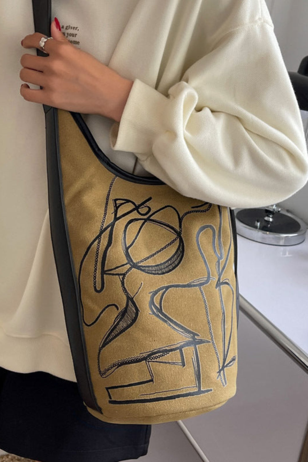 Person holding a tan bag with black abstract design in an indoor setting