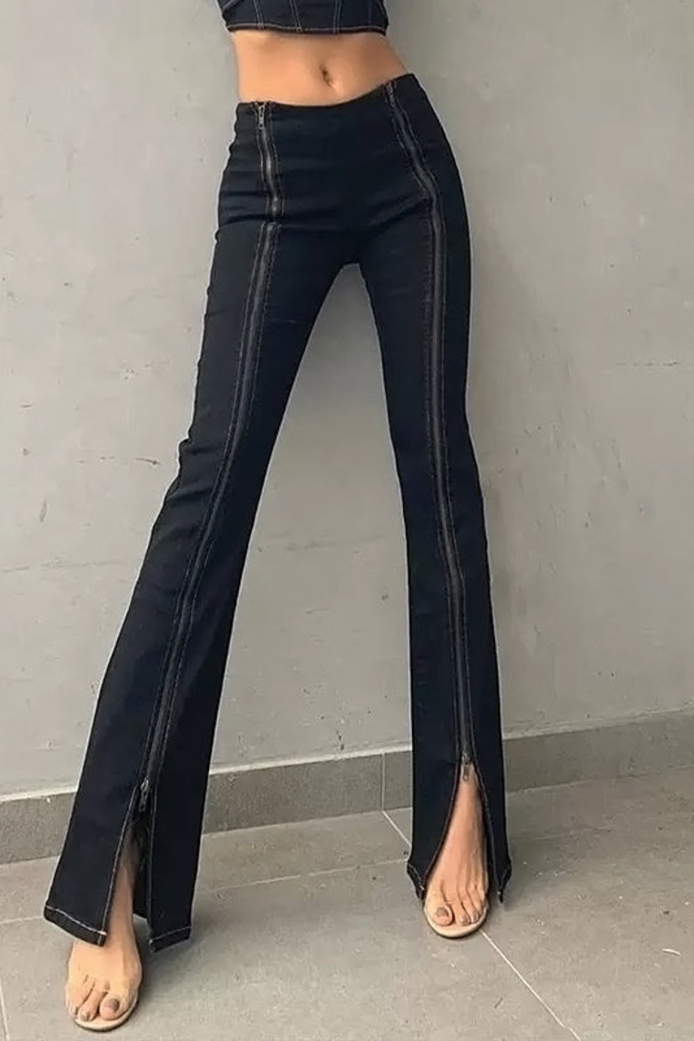 Black flared jeans worn by a person on a gray background