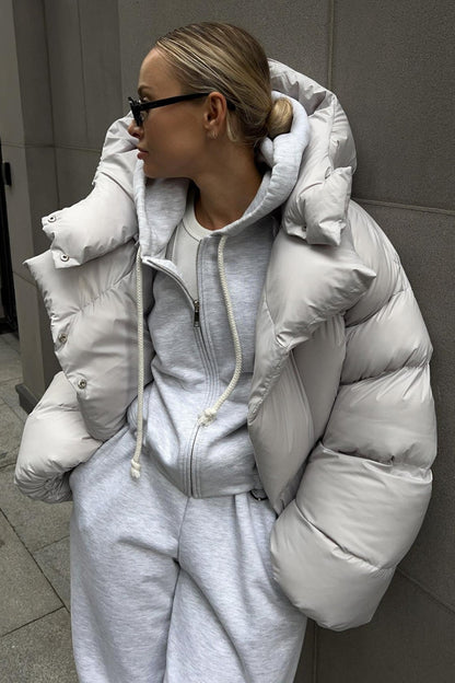 Person wearing a gray puffer jacket and matching tracksuit against a neutral background