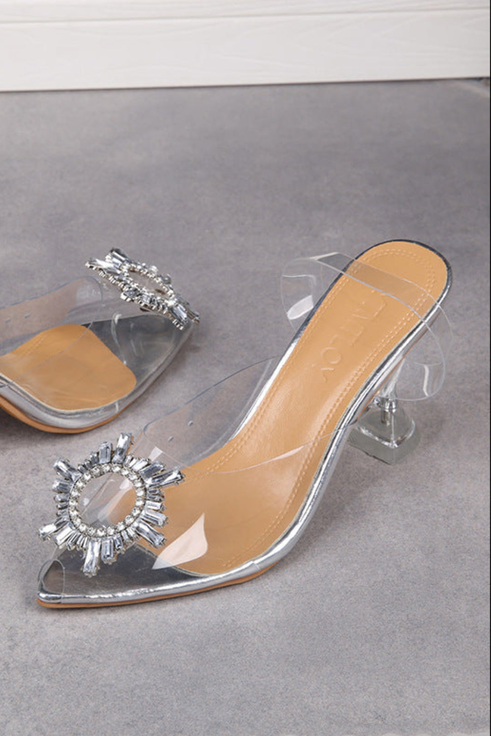 Clear high-heeled shoes with silver embellishments on a gray surface