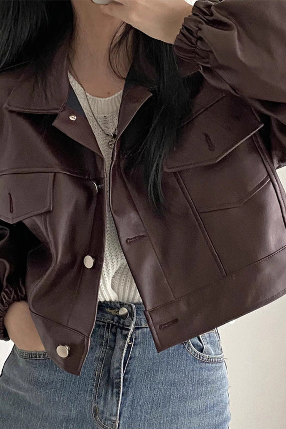 Person wearing a brown jacket and blue jeans against a neutral background