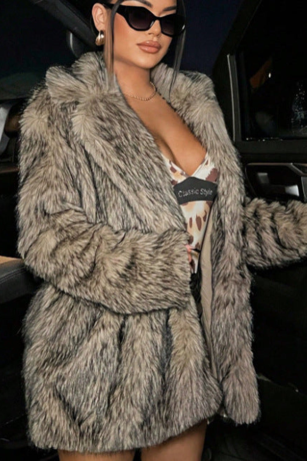 Person wearing a fur coat and sunglasses in a car.