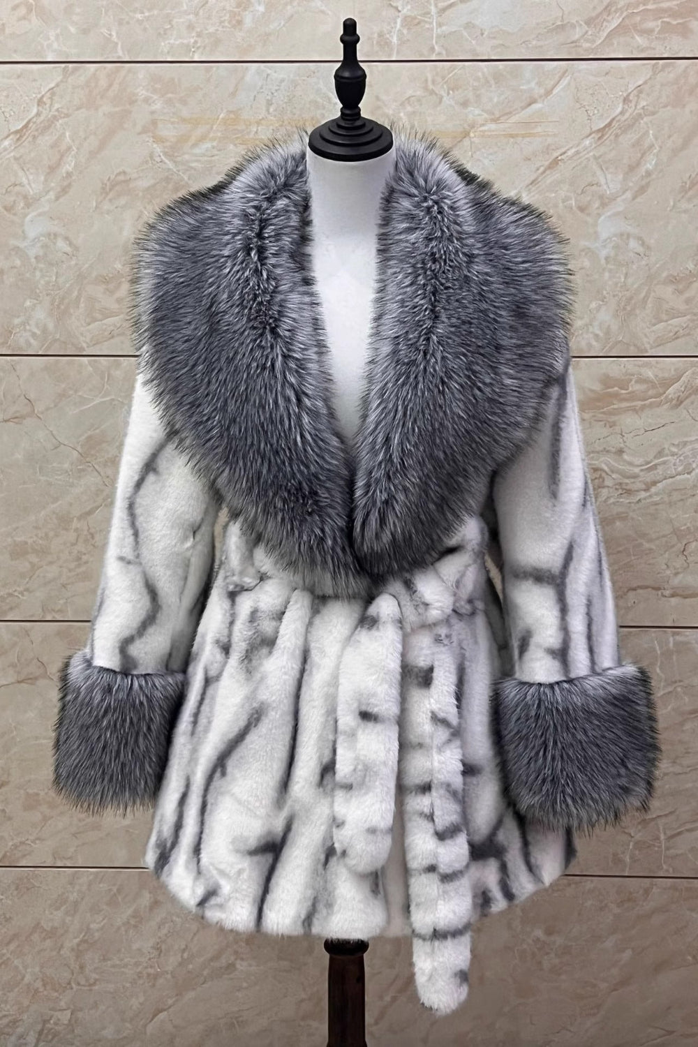 Fur-trimmed coat on a mannequin against a beige marble background