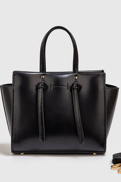Black handbag with a matching strap on a light gray background