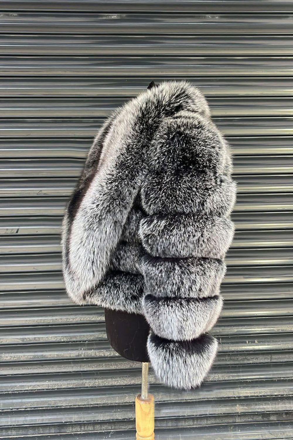 Gray fur coat with large hood on a stand against a metallic shutter background