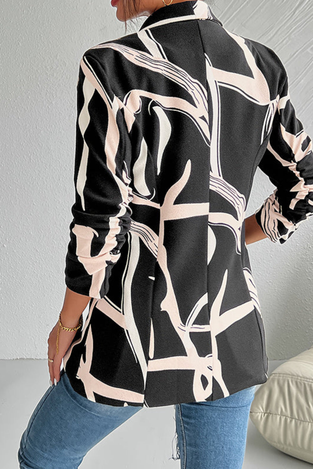 Person wearing a black and beige patterned shirt with blue jeans against a white wall.