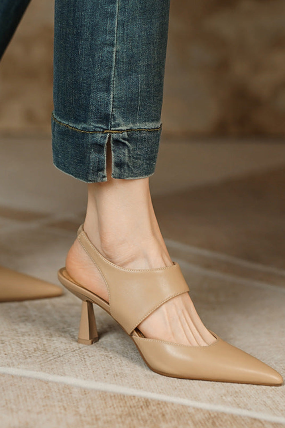 Beige high-heeled shoes worn with rolled-up jeans on a neutral background