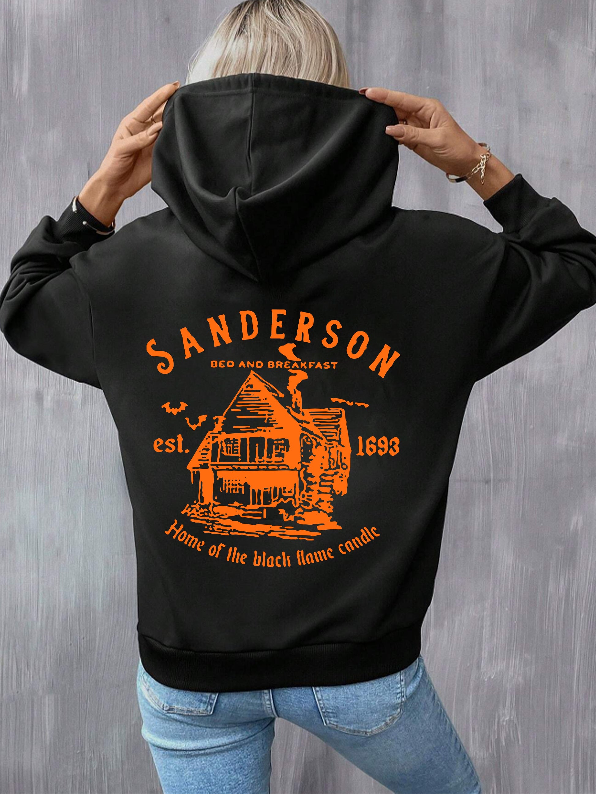 Person wearing a black hoodie with orange 'Sanderson Bed and Breakfast' design on the back against a gray background