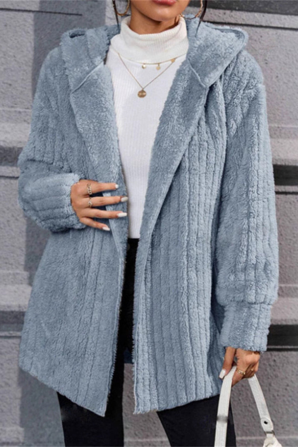 Person wearing a light blue textured coat with a white sweater underneath, standing on steps.