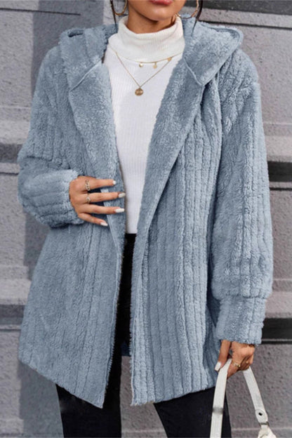 Person wearing a light blue textured coat with a white sweater underneath, standing on steps.