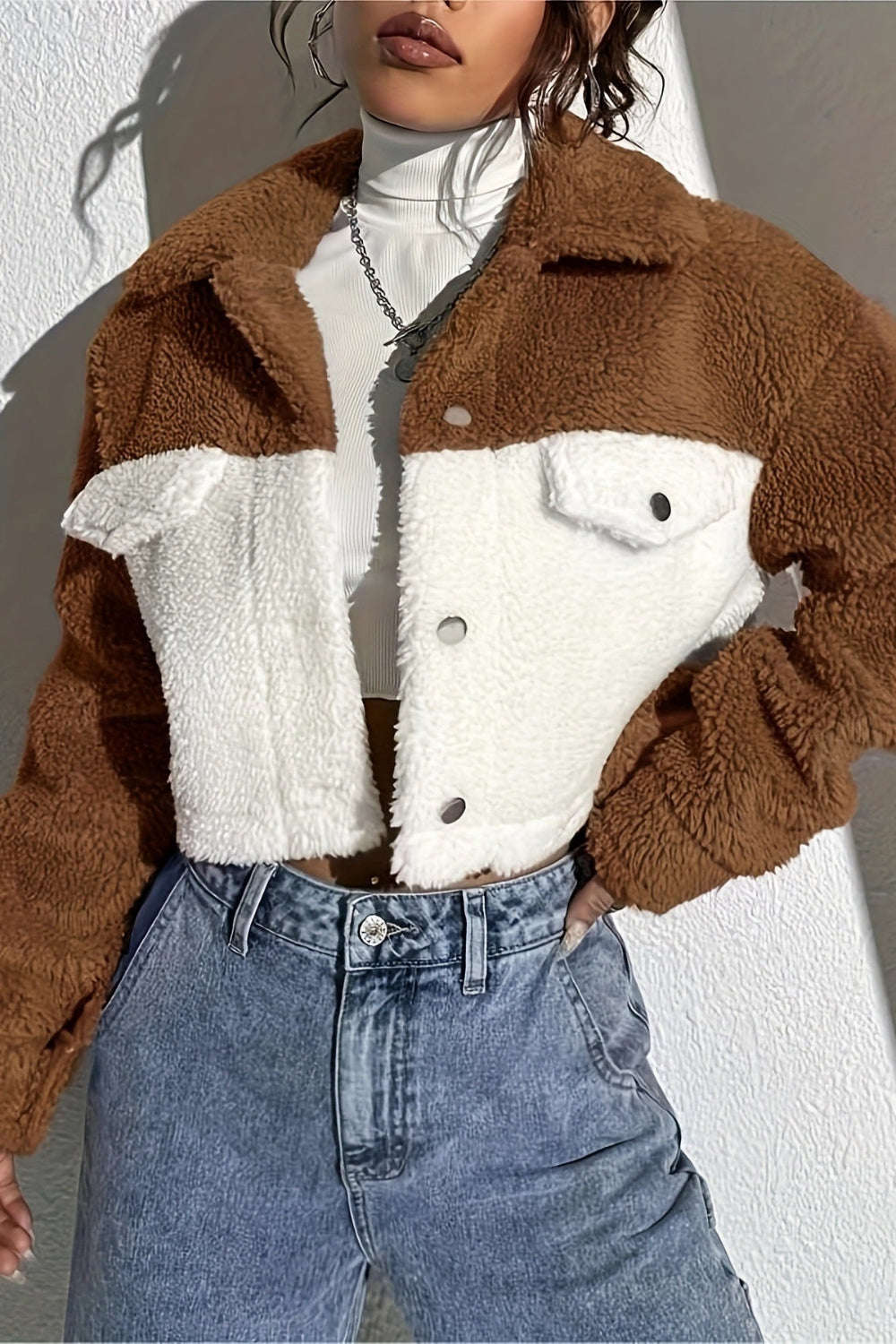 Person wearing a brown and white sherpa jacket with blue jeans against a neutral background