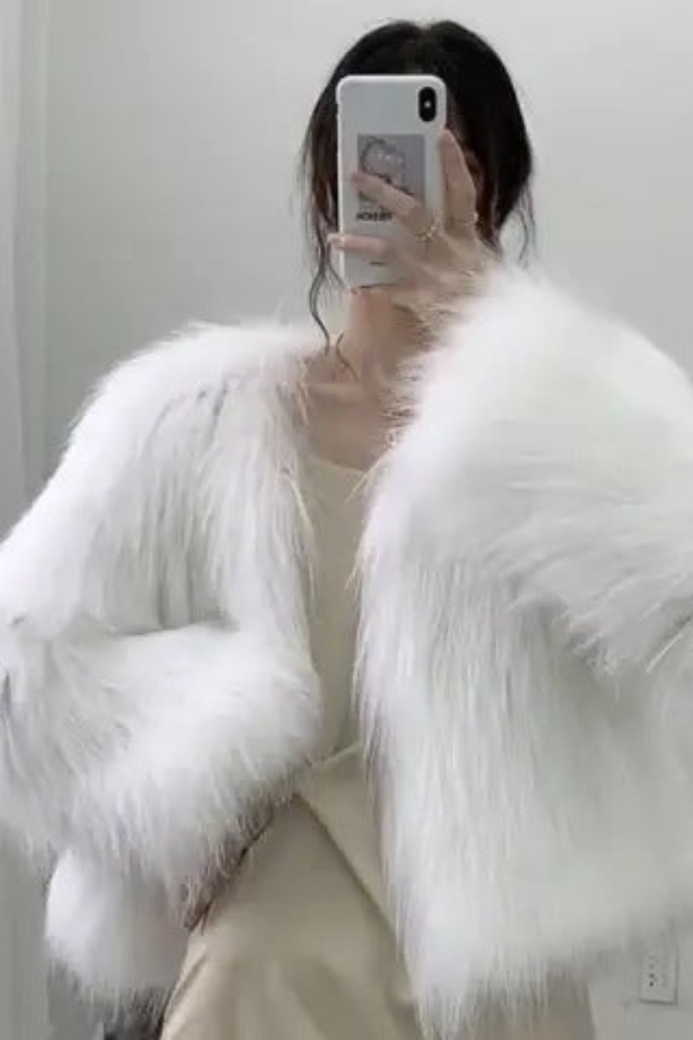 Person wearing a white fur coat taking a mirror selfie.