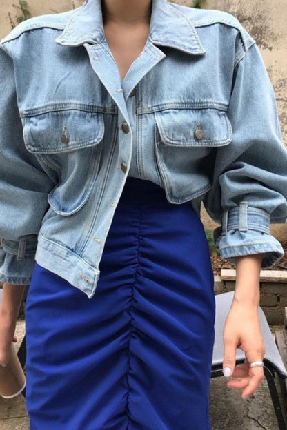 Person wearing a light blue denim jacket and blue pants sitting on a wooden pallet.