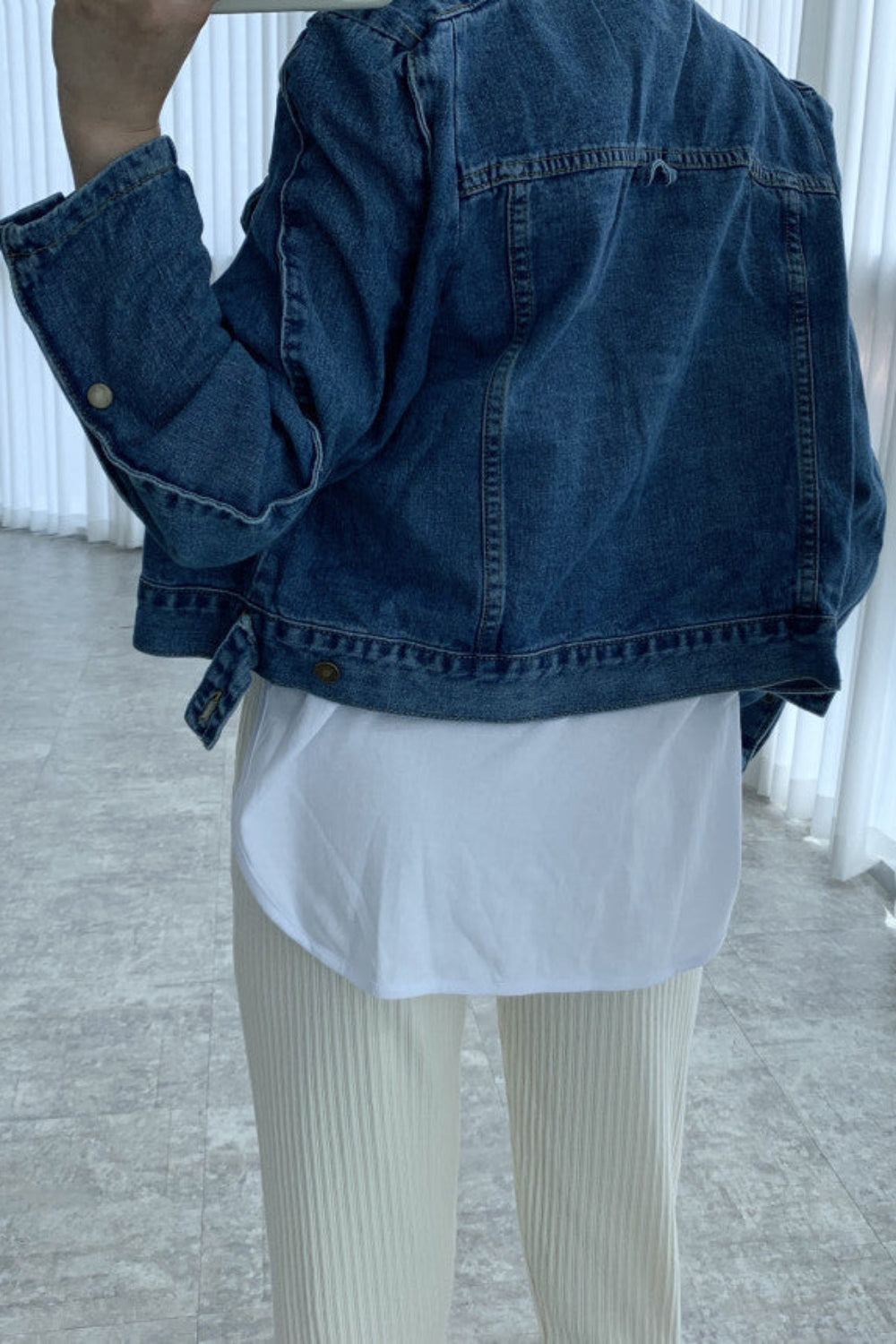 Person wearing a blue denim jacket over a white shirt and beige pants in an indoor setting.