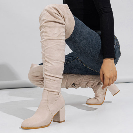 Beige knee-high boots worn by a person on a light gray background