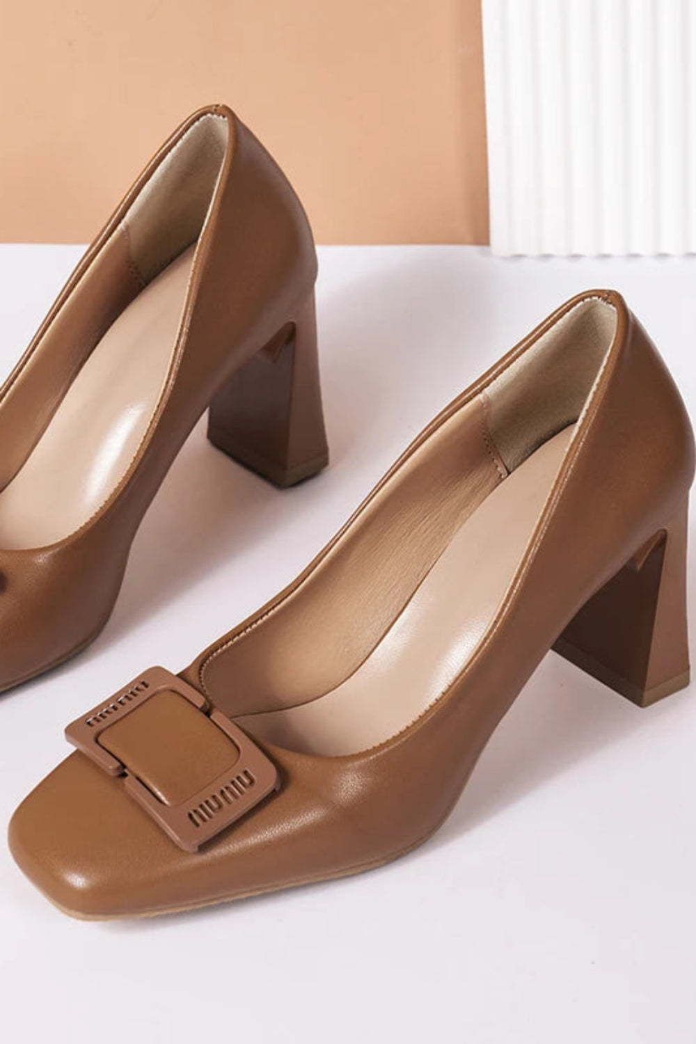 Pair of brown high-heeled shoes with a buckle on a white background