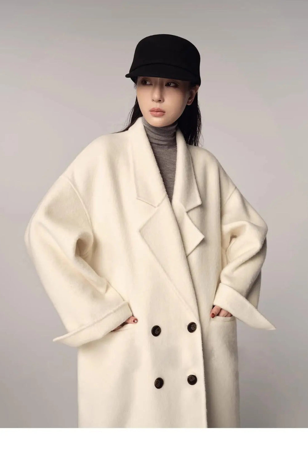 Person wearing a white coat with black buttons and a black cap on a plain background