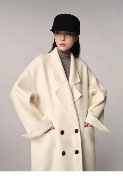 Person wearing a white coat with black buttons and a black cap on a plain background